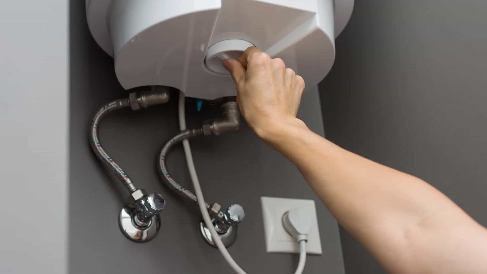 Mano ajustando un calentador de agua con sus conexiones de agua
