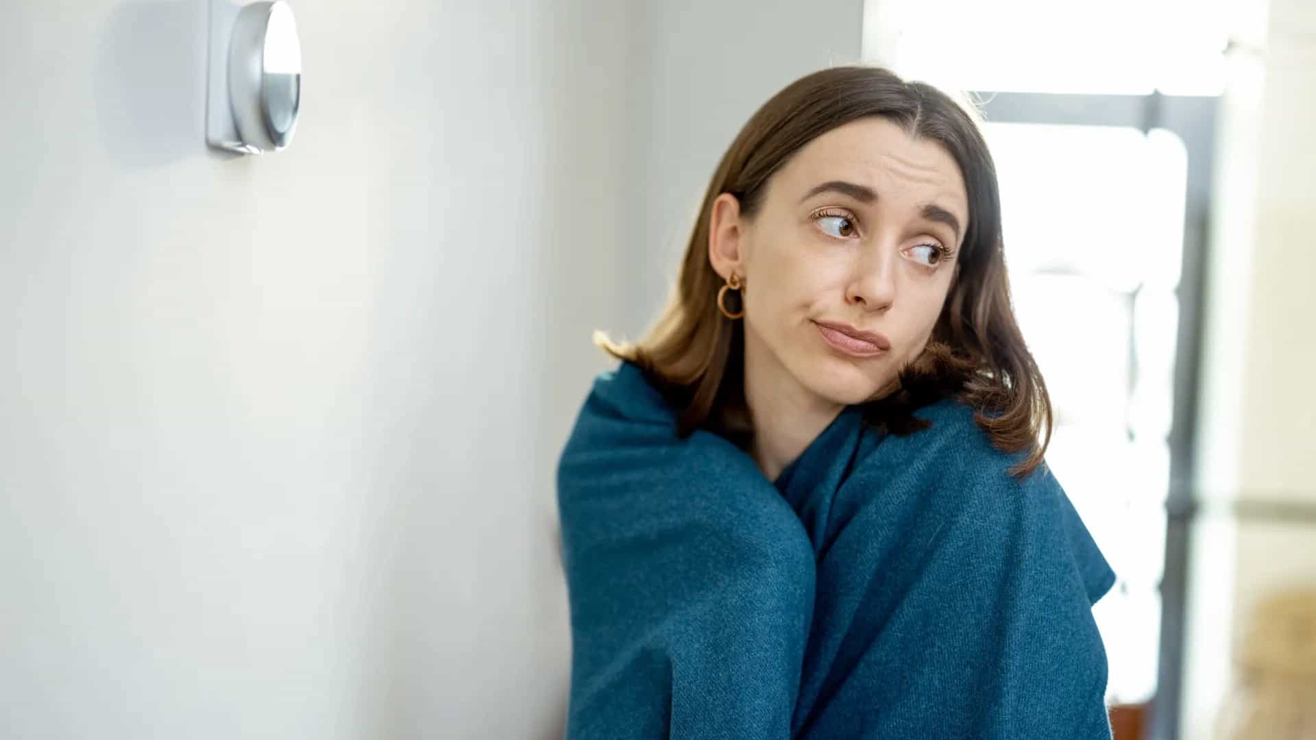 Mujer envuelta en una manta en casa por falta de calefacción