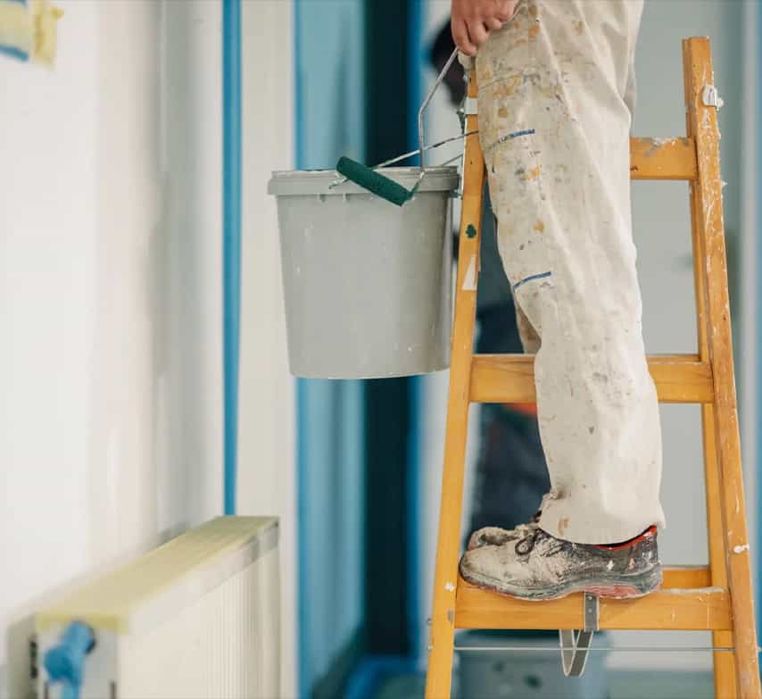 Pintor subido a una escalera con un cubo de pintura