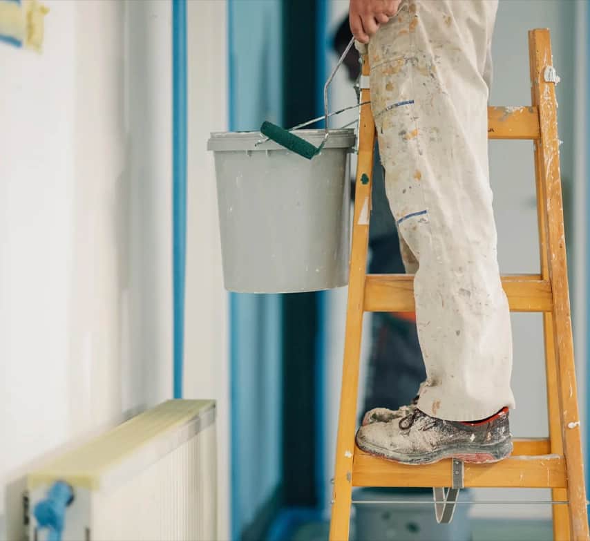 Pintor subido a una escalera con un cubo de pintura