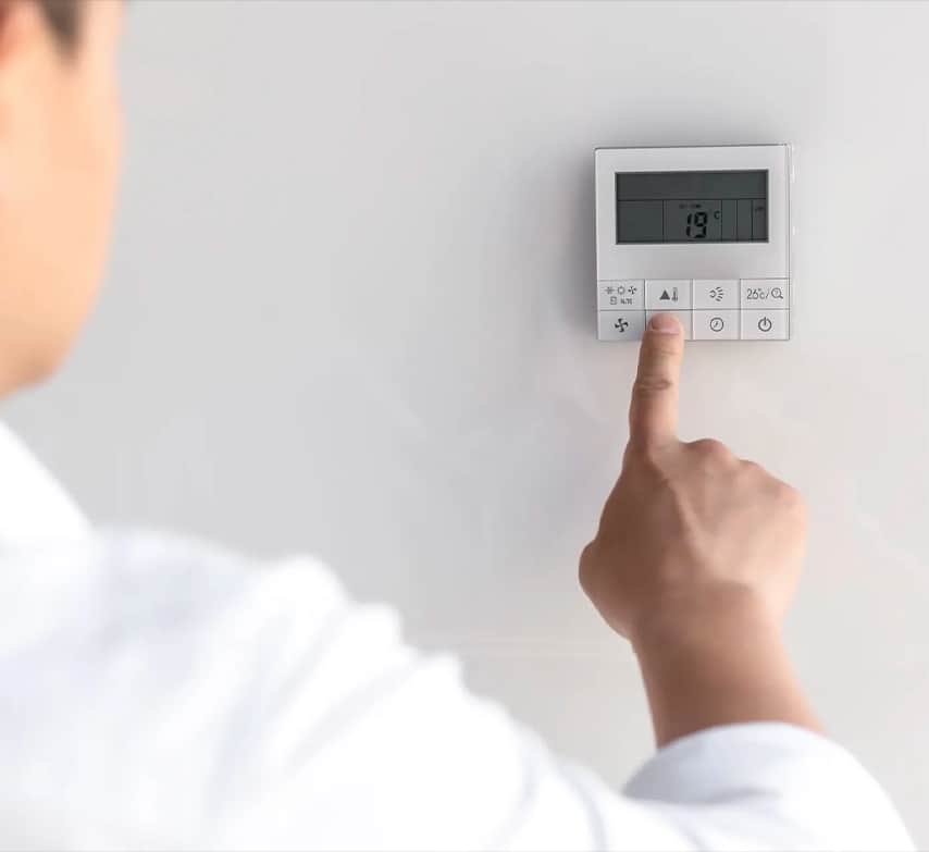 Dedo pulsando un termostato de pared de climatización