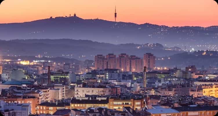 Vista al atardecer de una ciudad con la sierra y una torre de telecomunicaciones