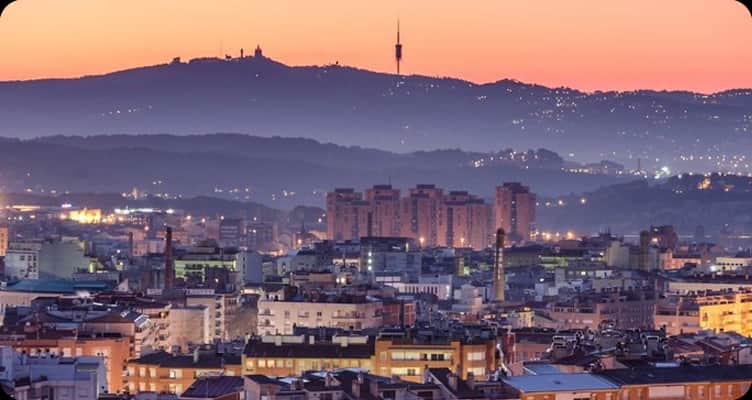 Vista al atardecer de una ciudad con la sierra y una torre de telecomunicaciones